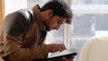 View of an Indian guy in a leather jacket sitting down and looking at his tablet at home Royalty Free Stock Photo