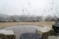 View from inside a hilltop home of a patio and subdivision below as rain falls. Taken through a rain spotted window.