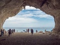 View from inside of limestone sea cave at Cala Luna beach, Sardinia, Italy with group of tourist people sunbathing and Royalty Free Stock Photo