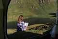 Young woman in front of a tent in the swiss mountains reading a book