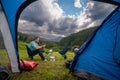 View from inside the tourist tent. The camp is ready for the night. Man is sitting in the portable chairs and at the table, dinner