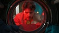 View from inside the washing machine, adult man looking angry inside the washer drum in red light