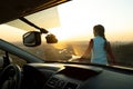 View from inside of a young woman standing near her car enjoying warm sunset view. Girl traveler leaning on vehicle hood looking Royalty Free Stock Photo