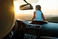 View from inside of a young woman standing near her car enjoying warm sunset view. Girl traveler leaning on vehicle hood looking Royalty Free Stock Photo