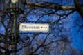 View on isolated direction sign with word museum in old german scripture on antique street lamp pole. Blurred bare tree and blue