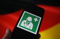 View on isolated mobile phone screen with international health and medical doctor symbol. Blurred waving german flag background. Royalty Free Stock Photo