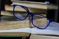 View on isolated stack of old yellowed books on wood table with blue reading glasses and open book Royalty Free Stock Photo