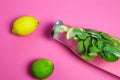 View on isolated water glass bottle flavored with mint leaves and yellow citrus, green lime fruit on pink background Royalty Free Stock Photo