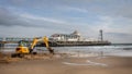 View of a JCB Excavator digging up the beach in front of Bournemouth Pier in Bournemouth, Dorset, UK