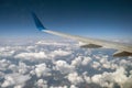 View of jet airplane wing from inside flying over white puffy clouds in blue sky. Travel and air transportation concept Royalty Free Stock Photo
