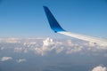 View of jet airplane wing from inside flying over white puffy clouds in blue sky. Travel and air transportation concept Royalty Free Stock Photo