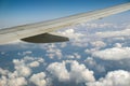 View of jet airplane wing from inside flying over white puffy clouds in blue sky. Travel and air transportation concept Royalty Free Stock Photo