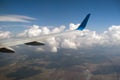 View of jet airplane wing from inside flying over white puffy clouds in blue sky. Travel and air transportation concept Royalty Free Stock Photo