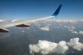 View of jet airplane wing from inside flying over white puffy clouds in blue sky. Travel and air transportation concept Royalty Free Stock Photo