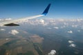 View of jet airplane wing from inside flying over white puffy clouds in blue sky. Travel and air transportation concept Royalty Free Stock Photo