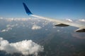 View of jet airplane wing from inside flying over white puffy clouds in blue sky. Travel and air transportation concept Royalty Free Stock Photo