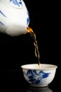 View of kettle pouring tea into china cup, black background, portrait Royalty Free Stock Photo