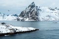 View of a landscape of a Norwegian fjord with a snowy mountain. In the foreground, on the rock is a small white house. Norway,