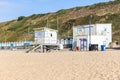 A view of a lifeguard tower on a sandy beach with beach huts and grassy cliff in the background under a beautiful blue sky Royalty Free Stock Photo