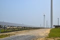 View of a long array of solar panels with an electric generating wind turbine in the background Royalty Free Stock Photo