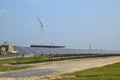 View of a long array of solar panels with an electric generating wind turbine in the background