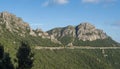 View of long open tunnel or viaduct with pillars and widows through limestone rock with green forest at Supramonte