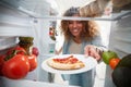 View Looking Out From Inside Of Refrigerator As Woman Opens Door For Leftover Takeaway Pizza Slice