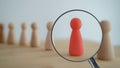 The view through the magnifier on the one wooden red person between other people. Resource management, recruitment, hire, headhunt