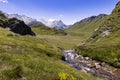 View of a majestic alpine landscape during a sunny day. In the foreground, a river winds, flowing between rocks and Royalty Free Stock Photo