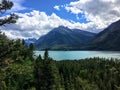 A view of a majestic turquoise lake surrounded by vast green evergreen forests and mountains on a sunny day with blue sky. Royalty Free Stock Photo