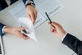 View of man gesturing near business partner giving envelope with money in office Royalty Free Stock Photo