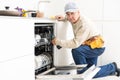 View Of Man In Overall Repairing Dishwasher In Kitchen Royalty Free Stock Photo