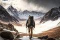 view of man, surrounded by the rugged beauty of a snowy mountain range, with his pack and trekking poles in hand