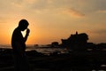 A man take of glasses in silhouette look at Pura Tanah lot, Bali, Indonesia.