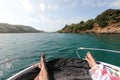 View on man and woman legs laying on yacht with tirquoise blue sea and beach with green palm trees on background. luxury Royalty Free Stock Photo