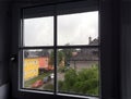 View from mansard window to city street with color houses and cars in rainy day