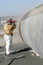 View of the manuel sandblasting to the large pipe. Abrasive blasting more commonly known as sandblasting is the operation.