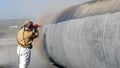 View of the manuel sandblasting to the large pipe. Abrasive blasting more commonly known as sandblasting is the operation.