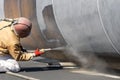 View of the manuel sandblasting to the large pipe. Abrasive blasting more commonly known as sandblasting is the operation.