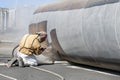 View of the manuel sandblasting to the large pipe. Abrasive blasting more commonly known as sandblasting is the operation.