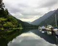 A view of a marina full of boats on a rainy grey day in at the end of remote, secluded inlet surrounded by forests and mountains.