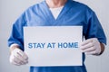 View of mature doctor holding placard with stay at home lettering on grey