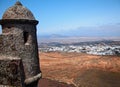 View from mediaeval fortress wall on hilltop. Village with white houses in the valley. Mountains and volcanoes on blue horizon