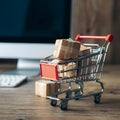 Miniature shopping cart with cardboard boxes, blurred computer screen background