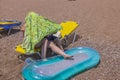 View of mother and child on sun lounger on sandy beach with air mattress for swimming, hiding from sun under towel. Royalty Free Stock Photo