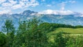 View of the mountain meadow with trees, grass and footpath and high mountains with snow-capped peaks in the distance