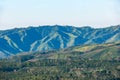 View of mountain ridges and sloping hills with trees under a clear blue sky