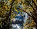 View of a mountain waterfall with turquoise water. In the foreground, trees with foliage frame the backstage scene. Autumn. Sunny Royalty Free Stock Photo