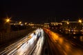 View of multilane urban highway with glowing lines of light from car headlamps and modern architecture