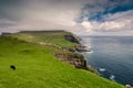 View on the Mykines island with moody clouds covering the top of the mountains and sheep grazing on the pasture, Mykines island, Royalty Free Stock Photo